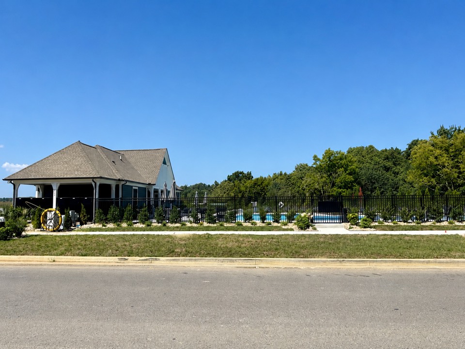 Street view of the Canebrake pool house, fenced pool, and surrounding landscaping